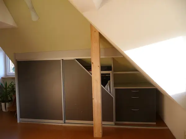 Ein maßgefertigter Einbauschrank mit Schiebetüren und Schubladen unter einer Dachschräge.