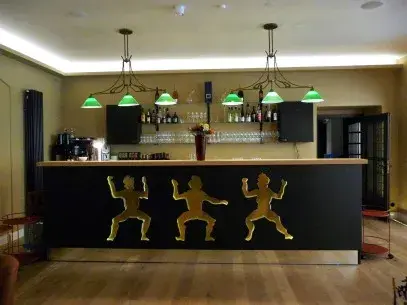 Moderne Bar mit Holztresen, goldenen Figuren und grünen Lampen im stilvollen Ambiente.