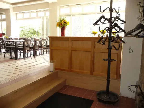 Heller Eingangsbereich eines Restaurants mit Garderobenständer, Holztresen und Blumenvasen.
