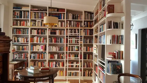 Gemütliche Bibliothek mit deckenhohen Bücherregalen, Leiter und Lesetisch voller Bücher.