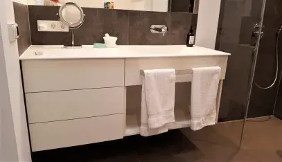 Modernes Badezimmer mit weißem Waschtisch, Spiegel und zwei Handtüchern vor dunkler Wand.