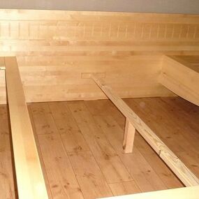 Massives Holzbettgestell mit großem Kopfteil und Ablagen auf Parkettboden im Schlafzimmer.