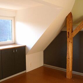 Dachgeschosszimmer mit Einbauschrank, Holzstütze und großem Fenster mit Tageslicht.
