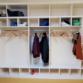 Offener Kleiderschrank mit Fächern, Kleiderstange, Kleidung, Jacken und Holzkleiderbügeln.